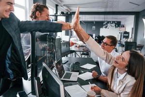 Giving high five. Team of stockbrokers works in modern office with many display screens photo