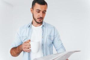 Reads newspaper. Young handsome man standing indoors against white background photo