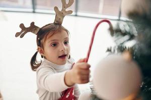 Cute little girl standing new New year tree with candy in hand photo