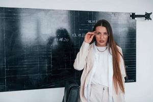 Young smart woman with glasses standing near blackboard photo