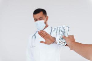 Medic won't take bribe. Young handsome man standing indoors against white background photo