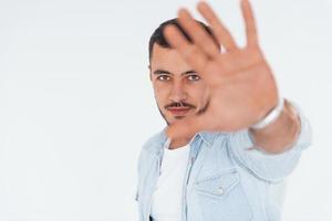 Stop gesture. Young handsome man standing indoors against white background photo