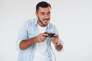 Holds joystick in hands. Young handsome man standing indoors against white background photo