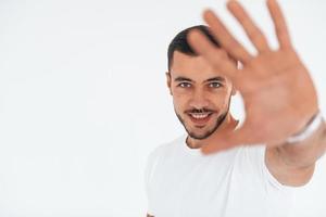 Stop gesture. Young handsome man standing indoors against white background photo