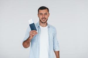 Tourist with ticket. Young handsome man standing indoors against white background photo