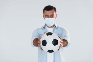 Football fan with soccer ball. Young handsome man standing indoors against white background photo