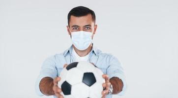 Football fan with soccer ball. Young handsome man standing indoors against white background photo