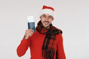 Holds airplane ticket. Young handsome man in New year clothes standing indoors against white background photo