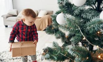 Cute little boy in festive clothes is indoors near christmas tree at New year time photo