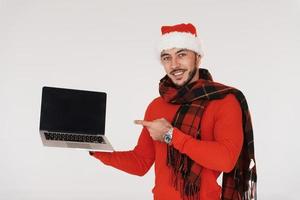 Holds laptop. Young handsome man in New year clothes standing indoors against white background photo