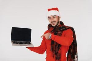 Holds laptop. Young handsome man in New year clothes standing indoors against white background photo