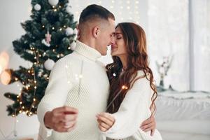 With sparklers in hands. Young romantic couple celebrates New year together indoors photo