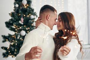 With sparklers in hands. Young romantic couple celebrates New year together indoors photo