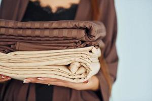 Close up view of young woman that standing against wall with bed clothes in hands photo