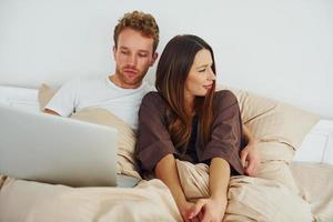 Couple lying down on bed with laptop. Interior and design of beautiful modern bedroom at daytime photo