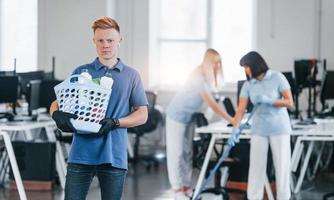 Woman uses vacuum cleaner. Group of workers clean modern office together at daytime photo