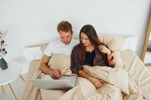 Couple lying down on bed with laptop. Interior and design of beautiful modern bedroom at daytime photo