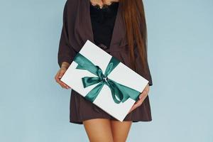 Close up view of young woman that standing against wall with gift box in hands photo