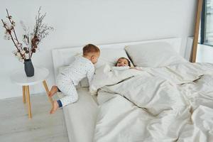 Two kids have fun while liyng down on bed. Interior and design of beautiful modern bedroom at daytime photo