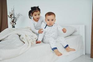 Two kids have fun while liyng down on bed. Interior and design of beautiful modern bedroom at daytime photo