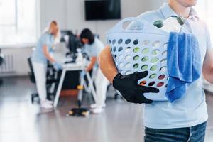 Man holds basket. Group of workers clean modern office together at daytime photo