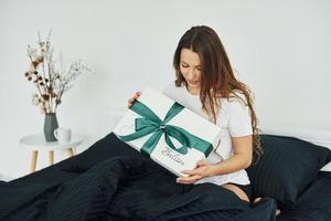 Gift box in hands of young woman. Interior and design of beautiful modern bedroom at daytime photo