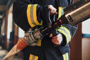 Hose in hands. Female firefighter in protective uniform standing near truck photo