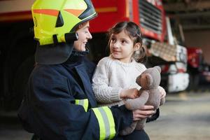 Happy little girl is with female firefighter in protective uniform photo