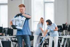 Woman uses vacuum cleaner. Group of workers clean modern office together at daytime photo