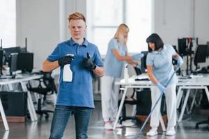 Woman uses vacuum cleaner. Group of workers clean modern office together at daytime photo