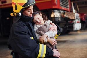 Happy little girl is with female firefighter in protective uniform photo