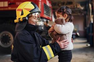 Happy little girl is with female firefighter in protective uniform photo