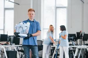 Woman uses vacuum cleaner. Group of workers clean modern office together at daytime photo