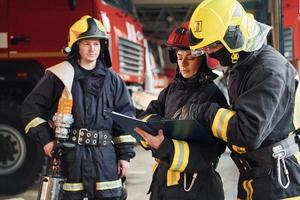 con bloc de notas grupo de bomberos con uniforme protector que está en la estación foto