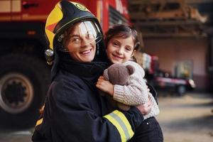 Happy little girl is with female firefighter in protective uniform photo