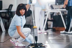 Woman uses vacuum cleaner. Group of workers clean modern office together at daytime photo