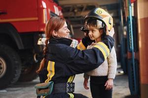 Happy little girl is with female firefighter in protective uniform photo