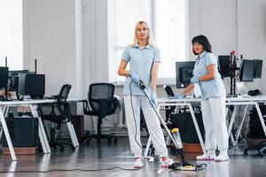 Woman uses vacuum cleaner. Group of workers clean modern office together at daytime photo