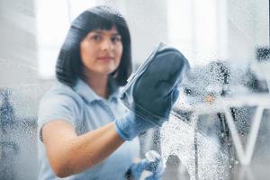 Woman cleaning dirty window by using towel. View through the glass photo