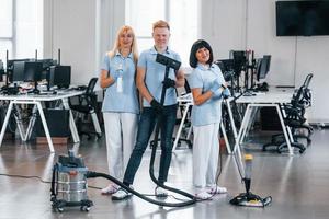 Guy with vacuum cleaner. Group of workers clean modern office together at daytime photo