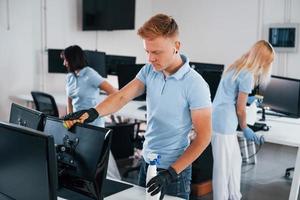 Cleans monitor. Group of workers clean modern office together at daytime photo