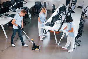 Cleans floor. Group of workers clean modern office together at daytime photo