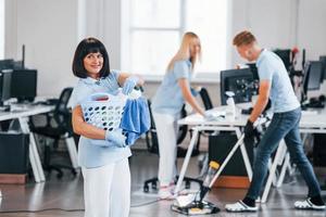 Woman with basket. Group of workers clean modern office together at daytime photo