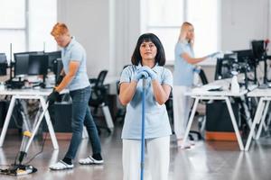 Cleans floor. Group of workers clean modern office together at daytime photo