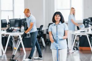 Cleans floor. Group of workers clean modern office together at daytime photo