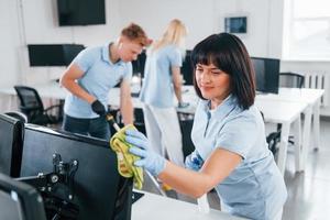 Cleans monitor. Group of workers clean modern office together at daytime photo