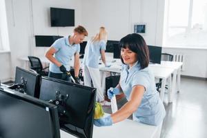 Cleans monitor. Group of workers clean modern office together at daytime photo