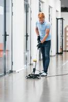 Young man works in the modern office. Uses vacuum cleaner photo