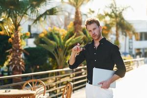 sostiene la computadora portátil. el joven está al aire libre durante el día soleado. concepto de vacaciones foto