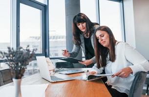 Two women in formal clothes is indoors in the modern office works together photo